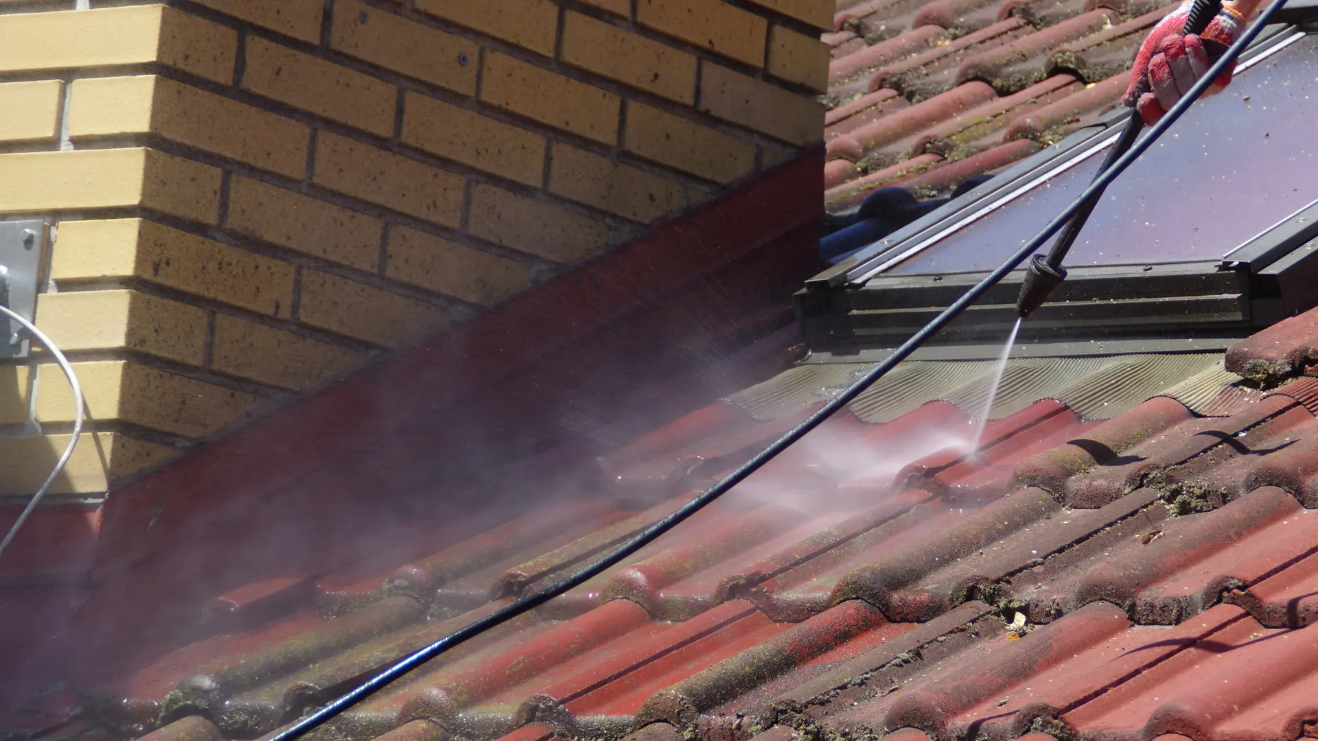 Moss and algae being washed from red roof tiles during a roof clean in Kent