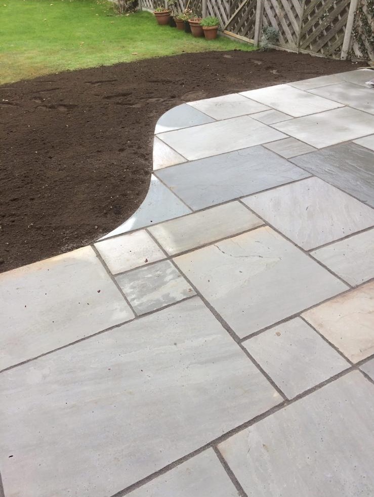 Grey sandstone patio with a curved lawn edge in Kent